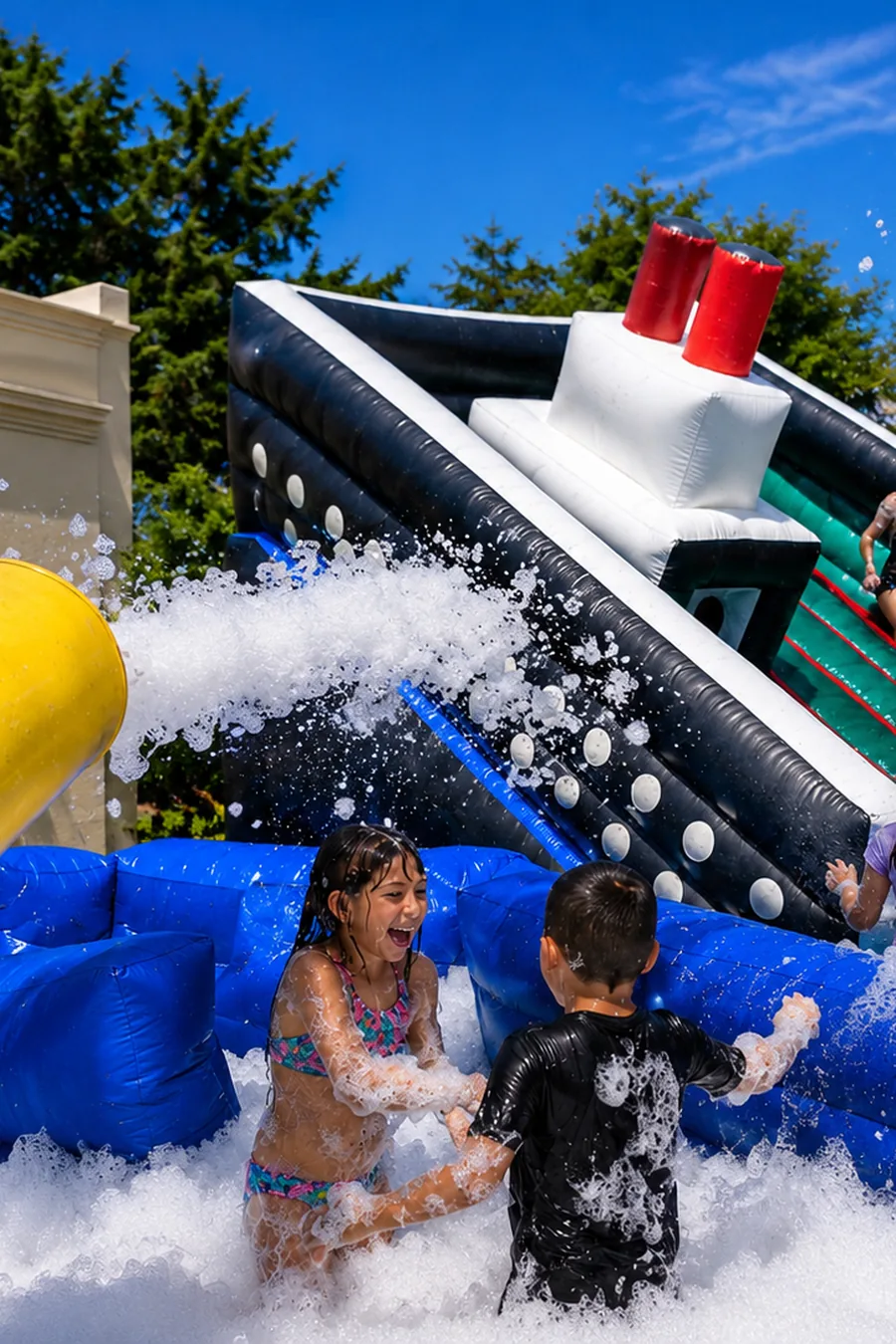 Niños jugando entre espuma junto a un cañón amarillo y un inflable